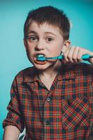 A cute boy in a pajamas brushes teeth with toothpaste before bedtime on a blue background photo