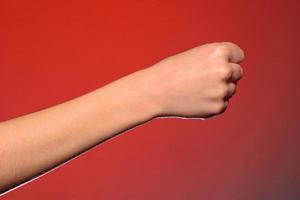 Human hand that squeezed fingers into a fist, symbolizing hatred and resistance, isolated on a red background photo