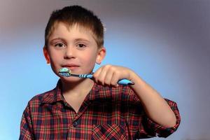 un hermoso niño pequeño en pijama sonríe y sostiene en su mano un cepillo de dientes sobre un fondo azul foto