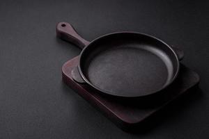 Empty round cast iron skillet on dark textured concrete background photo