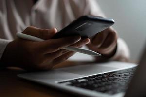 Business man facing laptop while looking at mobile phone photo