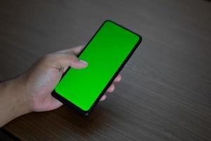 Hand holding smartphone with blank green screen for place user interface mockups photo