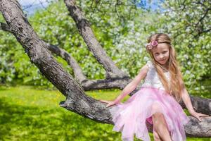 Little adorable girl sitting on blossoming tree in apple garden photo