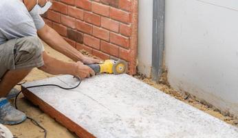 Close up worker holds Hand-Hold Sawing Machine and cuts brick foam plate board for wall installation. photo