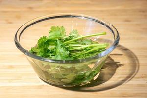 Close up with fresh coriander is prepared in a water glass bowl on wood plate background. photo