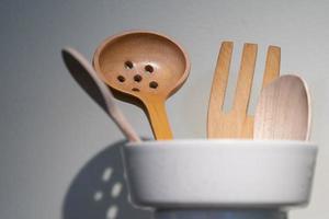 cerca de cucharón de madera, cuchara y tenedor en una taza blanca en el mostrador de la cocina. foto