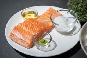 Salmon steak, Raw fillet of sea fish salmon or trout on white dish with salt, oil, and wasabi cream in studio light on dark background. photo