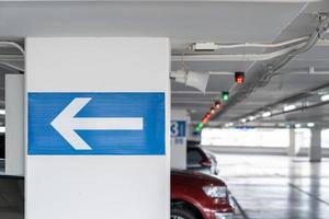 señalización de flecha blanca en el poste de estacionamiento interior, dígale al conductor qué camino tomar y ubicación en el estacionamiento. foto