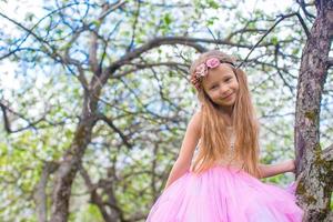 niña adorable sentada en un árbol floreciente en el jardín de manzanas foto