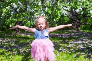 Adorable little girl in blooming apple tree garden on spring day photo