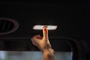 cierra un dedo pequeño de una niña de 5 años levanta la mano para encender y apagar la lámpara del camión en el techo del asiento trasero dentro del camión. foto