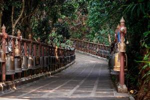 pasarela con campanas de bronce metálico alrededor y al lado en el entorno de la jungla, en el templo wat phra that doi tung, provincia de chiang rai, al norte de tailandia. foto