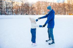 el padre joven y la niña adorable se divierten en la pista de patinaje al aire libre foto