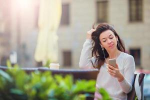 Young caucasian woman sending message and listen music in outdoor cafe photo