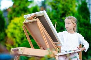 Adorable little girl painting a picture on easel outdoors photo