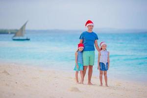 familia feliz con sombreros de santa en vacaciones de verano. vacaciones de navidad con una familia joven de cuatro personas disfrutando de su viaje por mar foto