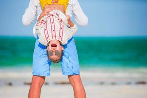 Happy father and his adorable little daughter at tropical beach having fun. Kid hanging upside down in the hands of her dad photo