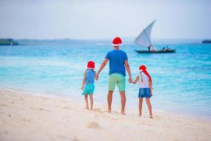 familia feliz con sombreros de santa en vacaciones de verano. vacaciones de navidad con una familia joven de cuatro personas disfrutando de su viaje por mar foto