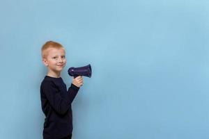 cute blond boy with megaphone smiling on blue background with copy space photo