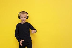 boy listens to music with headphones and dances on a yellow background with copy space photo