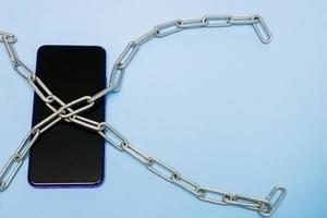 mobile phone in iron chains on a blue background with copy space photo