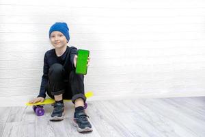 niño con un sombrero azul se sienta en una patineta sosteniendo un teléfono con una pantalla verde foto