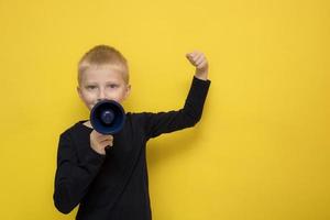 boy speaks life-affirmingly into a megaphone with a raised hand on a yellow background with copy space photo