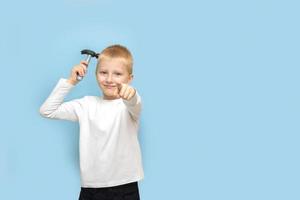 boy holding a hammer and pointing his finger forward with an ironic smirk on a blue background with copy space photo