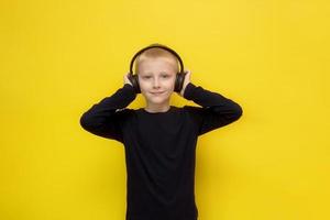 lindo chico rubio escuchando música o podcast en auriculares con fondo amarillo foto