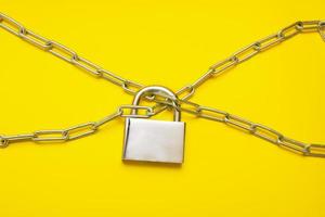 closed padlock hanging on chains on yellow background photo