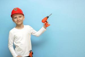 boy in a construction safety helmet with construction tools in his pocket holds a toy screwdriver in his hand on a blue background with copy space photo