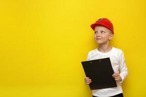 boy in a construction safety helmet with a tablet in his hands looks up on a yellow background with copy space photo
