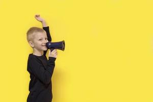 niño con una mano levantada con una sonrisa grita en un megáfono sobre un fondo amarillo con espacio de copia foto