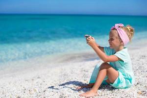 Little cute girl taking pictures on the phone at tropical beach photo