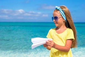 Happy little girl with paper airplane in hands on white sandy beach photo