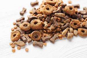 Dry food for dogs of different shapes on a white wooden background.