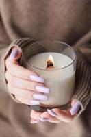 The hands of a young girl with a beautiful light purple manicure hold a candle photo