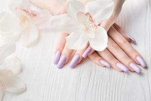 manos de niña con delicada manicura púrpura y flores de orquídeas foto