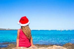 vista trasera de una linda niña con sombrero de santa en la playa foto