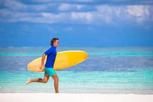 feliz joven surfista corriendo en la playa con una tabla de surf foto