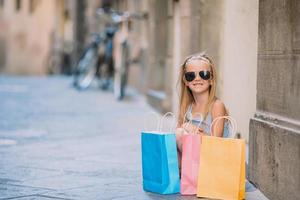 retrato de una adorable niña caminando con bolsas de compras al aire libre en una ciudad europea. foto