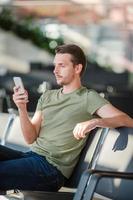 Passenger in a airport lounge waiting for flight aircraft. Young man with cellphone in airport waiting for landing photo