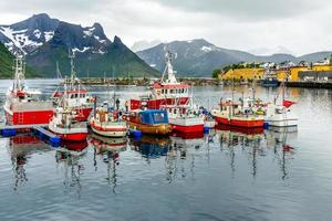 barcos de pesca en el muelle con la montaña al fondo en el pueblo de husoy, isla senja, noruega foto