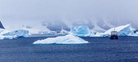 Snowfall and cruise ship among blue icebergs in Port Charcot, Booth Island, Antarctic photo
