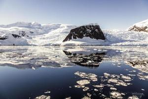 Snow rock and the glacier reflected in the Antarctic waters with icebergs of Neco bay, Antarctica photo