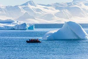 Boat full of tourists passing by the huge icebergs in the bay near Cuverville island, Antarctic peninsula