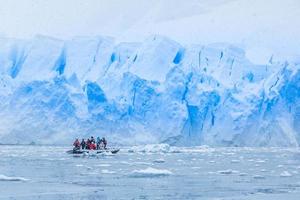 nevadas sobre un barco con turistas en la bahía llena de icebergs con una enorme pared glaciar en el fondo, cerca de almirante brown, península antártica foto