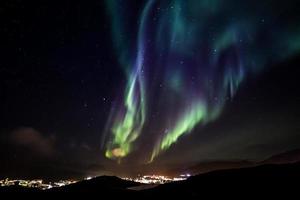 Glows of Northern Lights with shining stars on the sky over the mountains and highlighted city, Nuuk, Greenland photo