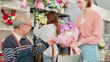 empresario de negocios sin efectivo. Mujer cliente blanca comprando y pagando digitalmente escaneando una aplicación de teléfono móvil a un anciano asiático dueño de una floristería. hermosa tienda de flores, tienda sme inteligente. video