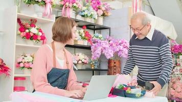 bargeldloser Unternehmer. asiatischer älterer männlicher kundenshop und digitale zahlungen durch scannen einer handyanwendung an eine weiße floristenbesitzerin. schöner Blumenladen, schicker KMU-Laden. video